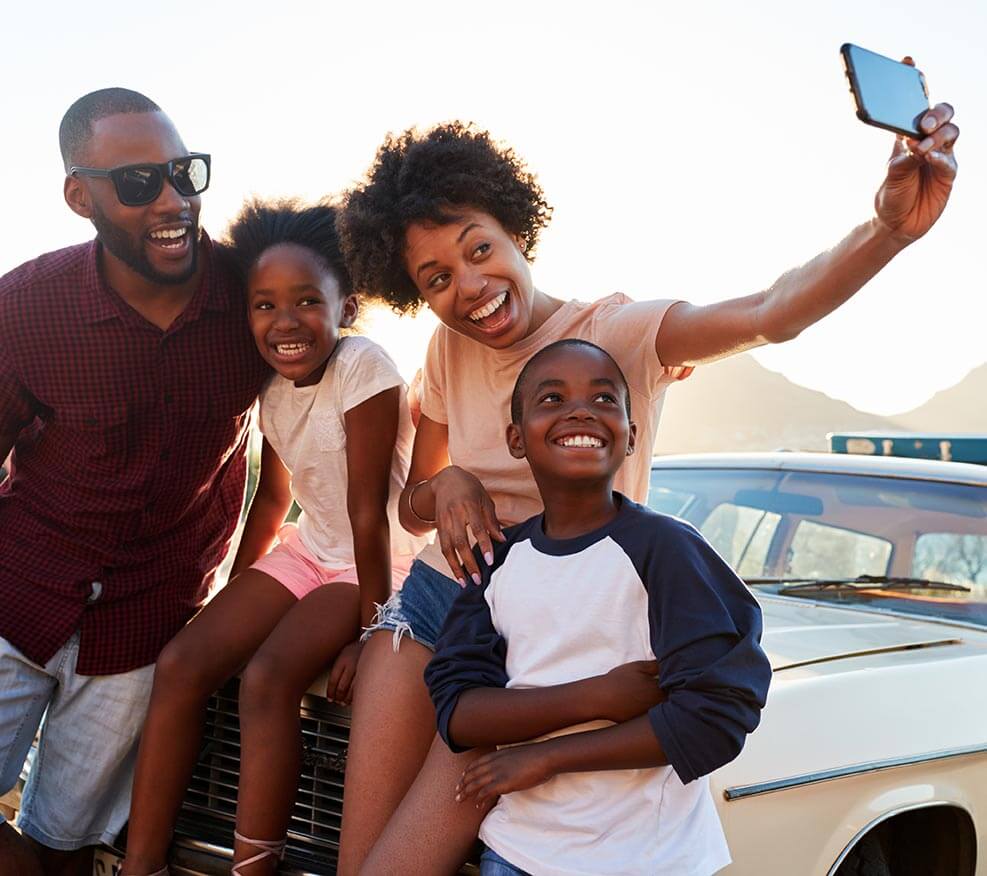 Young family taking a selfie with a car in the background