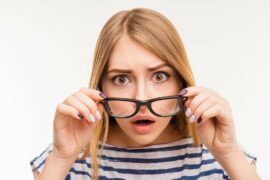 woman peering over black rimmed glasses with surprised expression
