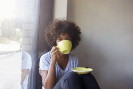 Woman sitting casually holding saucer plate and gazing over coffee while taking a sip from mug