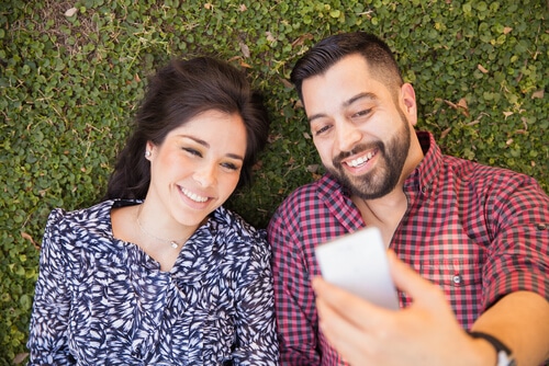 Man and woman taking selfie while laying on the grass