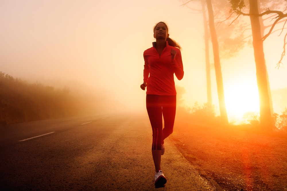 woman jogging in morning light, along road with trees