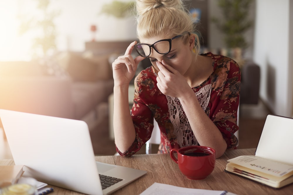 Woman in front of a laptop rubbing her eyes