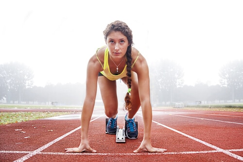 Female runner on track at starting block in ready position to begin a race