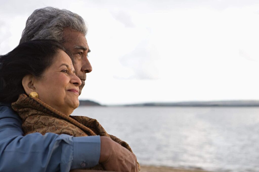 Older man and woman embracing with ocean in the background