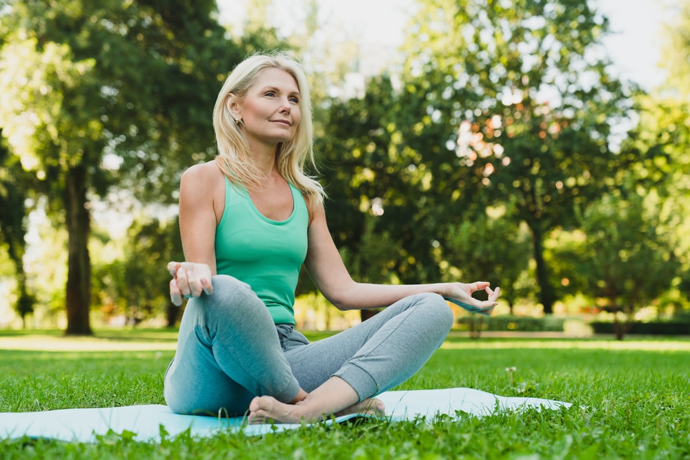 Middle-aged blonde woman happily doing yoga in the park.
