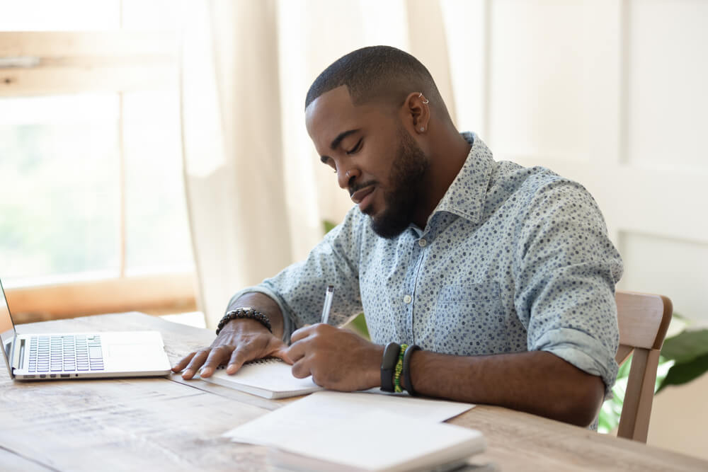 Man writing in a notebook with an open laptop