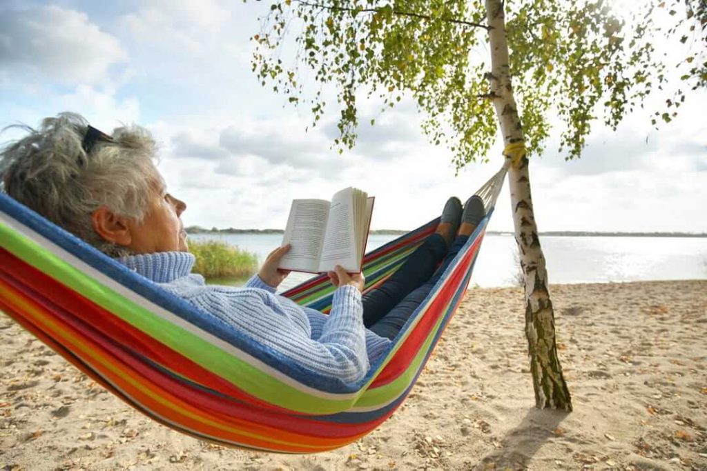 Older woman in hammock reading a book on the beach