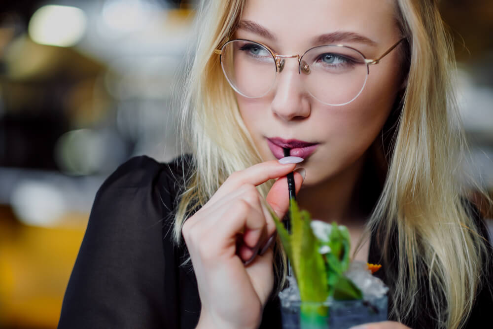 Stylish young blonde haired woman with glasses drinking from a straw