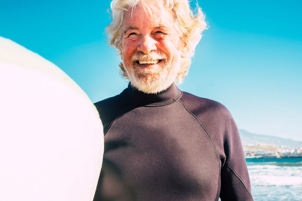 Smiling older man holding a surfboard at the beach