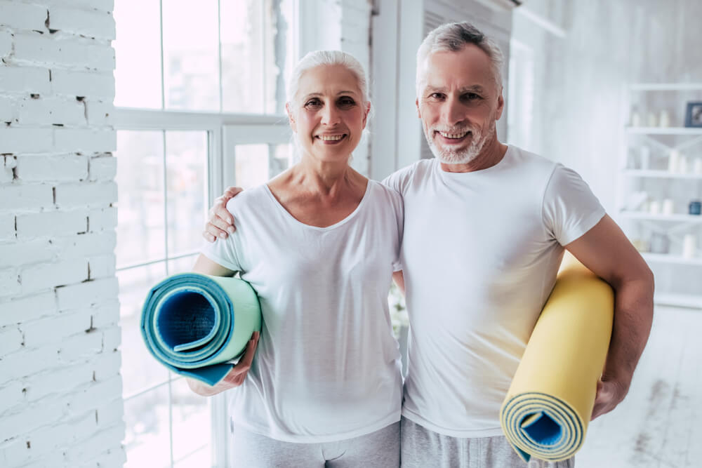 Happy older couple both holding rolled up yoga mats